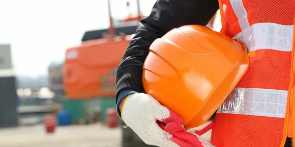 Person in safety vest holding an orange helmet