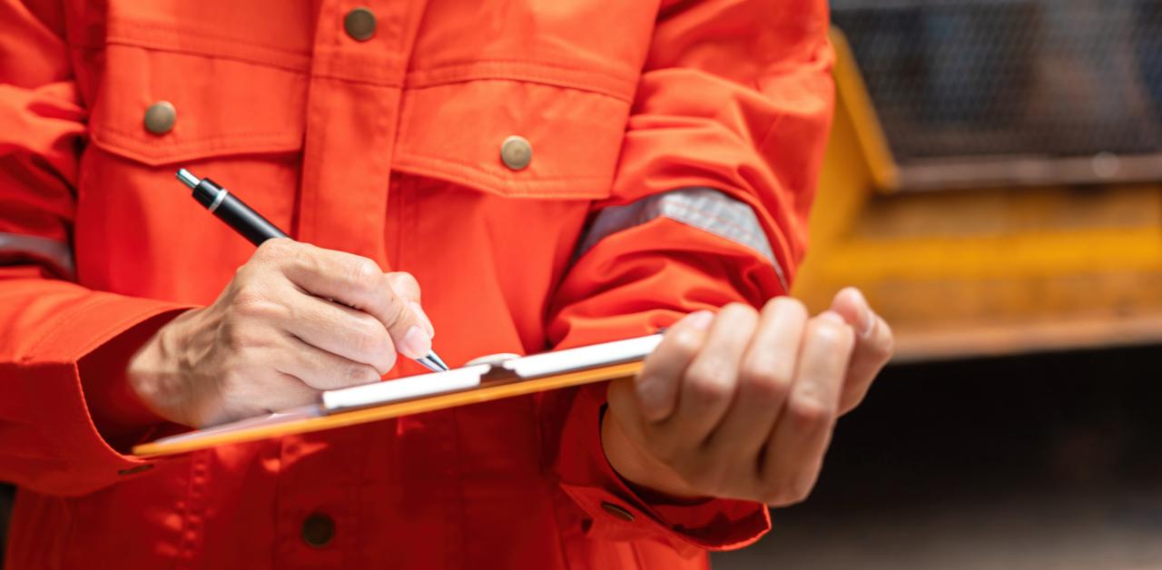 Person in safety orange shirt writing on a clipboard